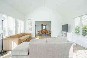 Un salón espacioso con techo alto, una zona de comedor con mesa y sillas, y un televisor sobre un mueble.