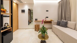 A modern living room with a sofa, a coffee table, a potted plant, and a wooden shelf with kitchen items. - The Wine Hotel (Rhodes)