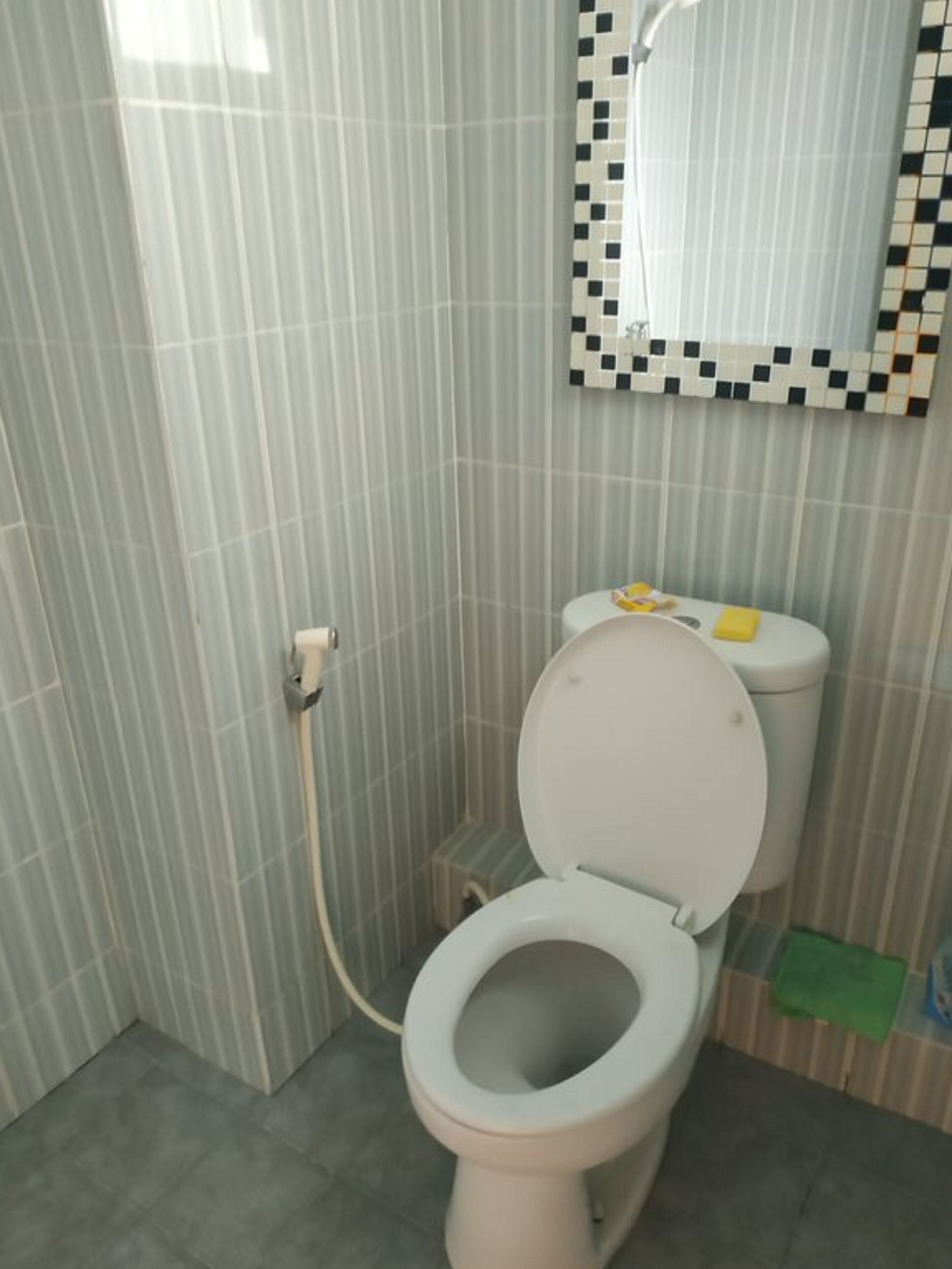 A bathroom with a toilet, a mirror, and a tiled wall.