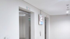 Een schone, moderne hal met twee liften en een digitaal informatiepaneel.