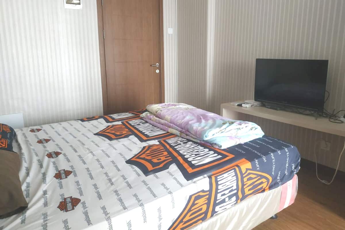 A bedroom with a bed, a television on a stand, and a door.