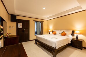 Una habitación de hotel con una cama grande, lámparas de noche, una mesita de noche de madera, un escritorio con un jarrón de flores y una puerta con espejo.