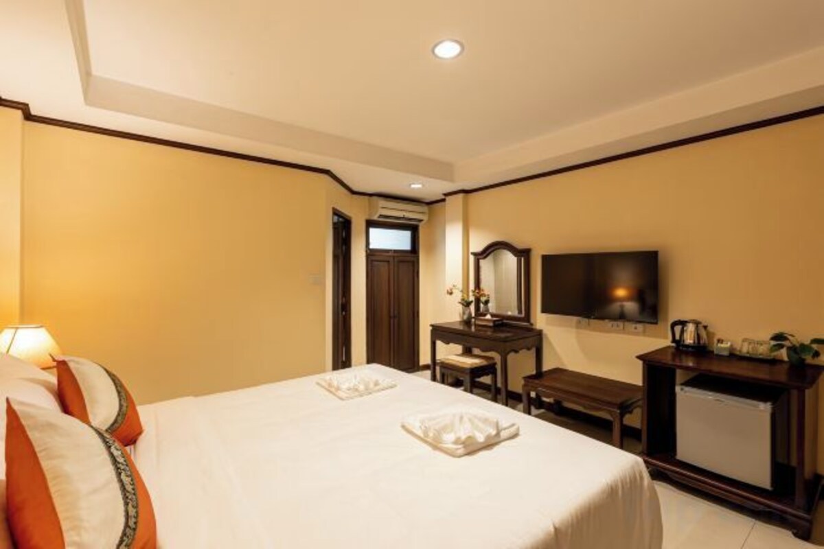 A hotel room with a bed, bedside table, lamp, and a television.