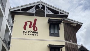A building with a beige facade, a prominent logo with Thai script, and a traditional Thai architectural design at the top. - Na Thapae Chiangmai Hotel (Chiang Mai)