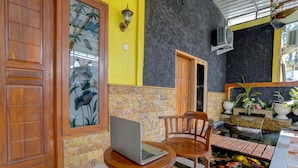 A room with a wooden door, a glass door with floral patterns, a laptop on a small table, a wooden chair, and a koi pond. - OYO Life 92840 Wisma Morricco  (Jogoroto)