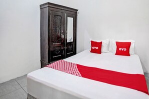 Una habitación de hotel con una cama, dos almohadas rojas, un armario de madera oscura y una pared blanca.