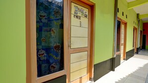 A hallway with green walls and doors, one with a sticker board and another with a window decorated with cartoon characters. - OYO Life 92840 Wisma Morricco  (Jogoroto)
