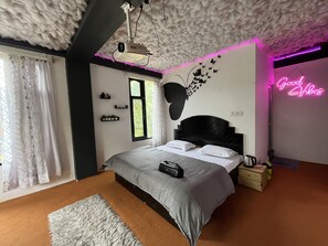 A modern bedroom with a bed, a ceiling projector, a window with curtains, a wall-mounted shelf with plants, and a neon sign. - The Locals By Roomshala (Manali)