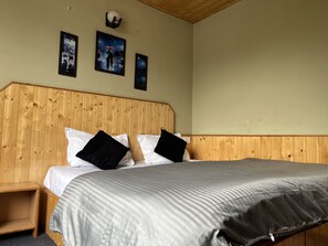 A room with a wooden headboard, a bed with white and black pillows, and three framed paintings on the wall. - The Locals By Roomshala (Manali)