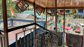 Un espace extérieur abrité, doté d’un plafond en bois, d’une rambarde en métal et offrant une vue sur un quartier résidentiel, avec des drapeaux colorés et un mât.