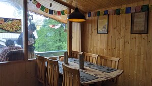 Un intérieur en bois avec une table et des chaises, un luminaire suspendu et une fenêtre donnant sur un paysage verdoyant.