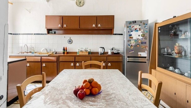 Una cocina con armarios de madera, un refrigerador con imanes, una mesa de comedor con sillas y un salpicadero de azulejos.