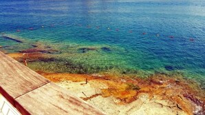 Una vista despejada de una playa con una terraza de madera y un litoral rocoso.