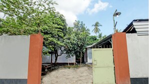 A gated entrance with a green gate, a dirt path leading to a covered area, and a street lamp. - OYO Life 93058 Kos Subur (Tanjung)