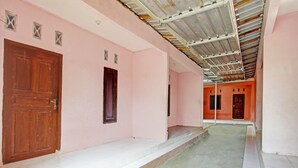 A corridor with pink walls, wooden doors, and a tiled floor. - OYO Life 93058 Kos Subur (Tanjung)