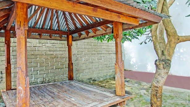 A wooden pergola structure with a bench underneath, set against a brick wall and a tree. - OYO Life 93058 Kos Subur (Tanjung)