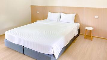A neatly made bed with white linens, a wooden headboard, and a small wooden stool beside it.