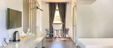 A hotel room with a bed, a desk with a flat-screen TV, a coffee maker, and a table with chairs.