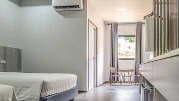 A modern hotel room with a bed, a small table with chairs, an air conditioning unit, and a window with curtains.