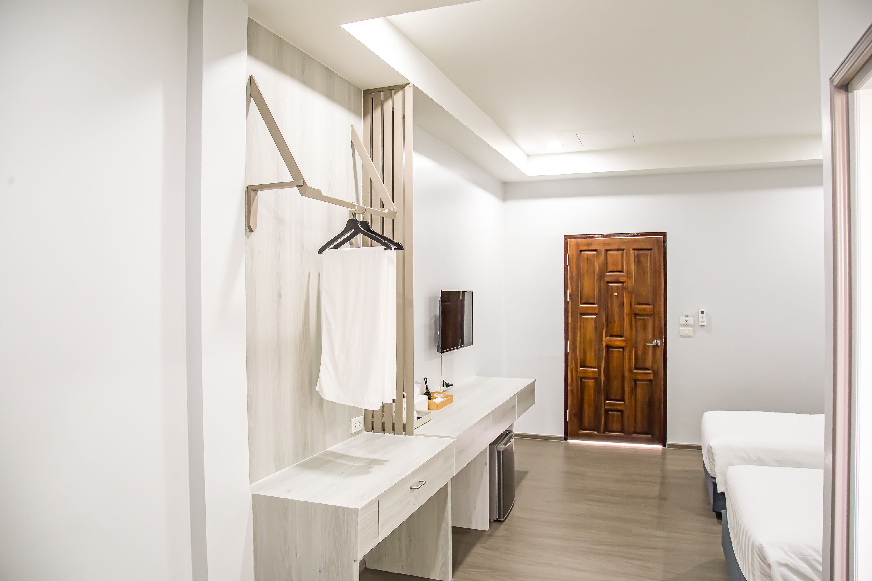 Una habitación de hotel moderna con una puerta de madera, un tocador largo y blanco con espejo, y un televisor de pantalla plana montado en la pared.