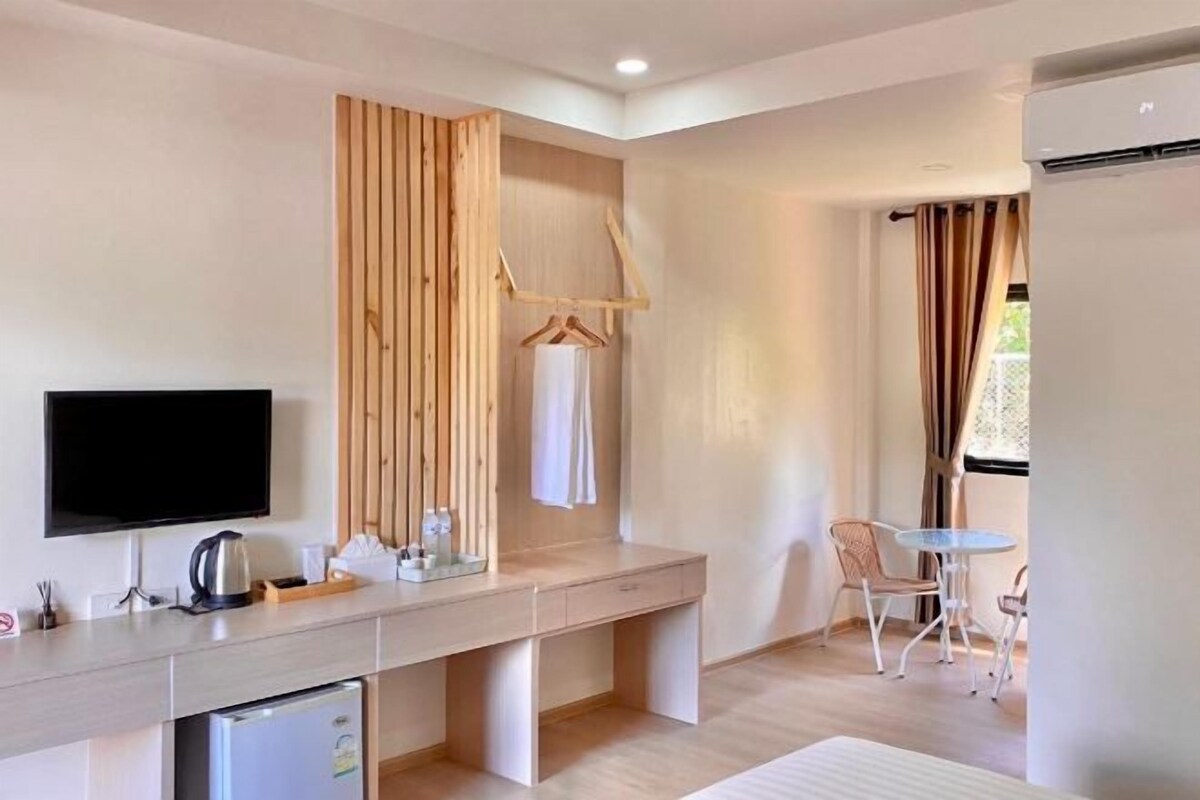 A modern hotel room with a wooden desk, a television, a small refrigerator, and a seating area with chairs and a table.