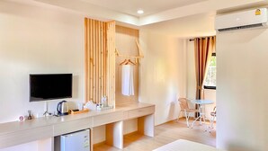 A modern hotel room with a wooden desk, a television, a mini-fridge, a small table with chairs, and a window with curtains. - น่าน ม่วนใจ Nan Muanjai Hotel (Pua)