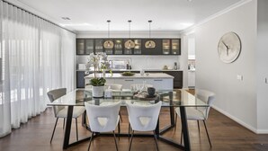 Una cocina moderna con una mesa de comedor de vidrio, sillas blancas y lámparas colgantes.