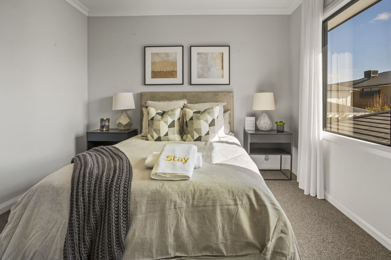 Une chambre d’hôtel avec un lit, deux tables de chevet, une fenêtre avec des rideaux et deux tableaux encadrés accrochés au mur.