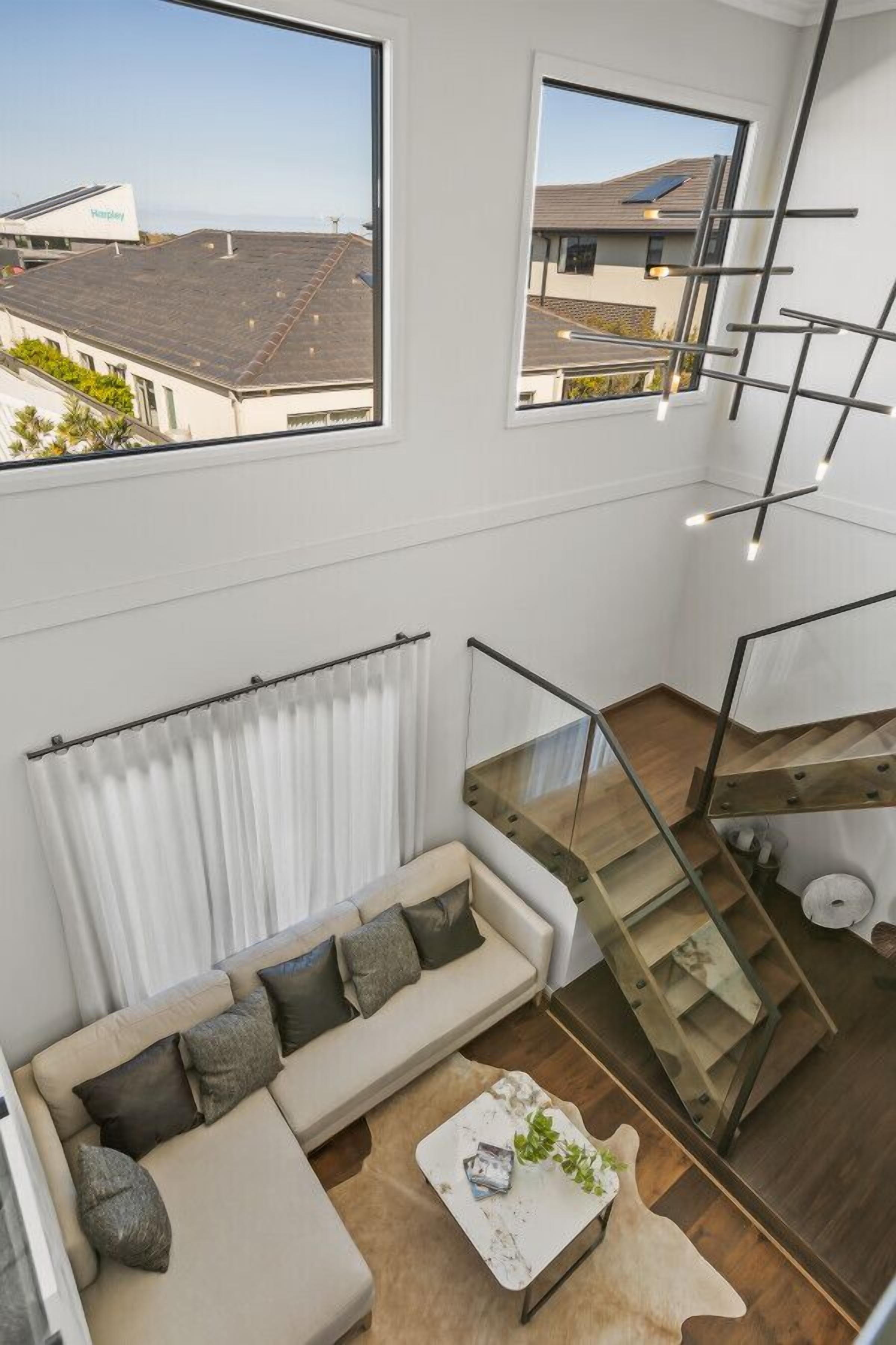A modern interior with a sofa, a coffee table, a staircase, and large windows.