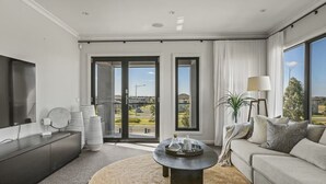 Un salón moderno con un sofá, una mesa de centro y un televisor. Dos amplias puertas correderas dan acceso a un balcón.