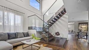 Una sala de estar moderna con un sofá, una mesa de centro y una escalera con barandillas de vidrio.