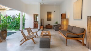 Un salon spacieux comprenant un canapé, deux fauteuils, une table basse et une grande plante en pot.