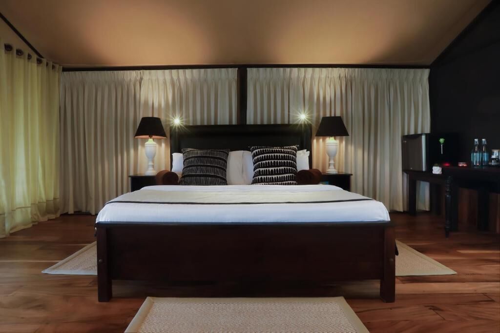 A large bed with a dark headboard, two bedside lamps, and a nightstand with a lamp.
