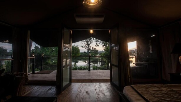 A room with a bed, a wooden deck, and a view of a lake. - Leopard Trails Yala (Kataragama)