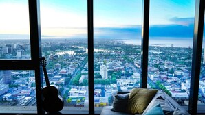 Blick auf die Stadtlandschaft aus einem Hochhausfenster, mit einer Gitarre auf einer Fensterbank und einem Sofa mit Kissen.