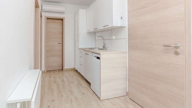 A compact kitchen with white cabinets, a dishwasher, and a sink. - Apartments Budimir (Vir)