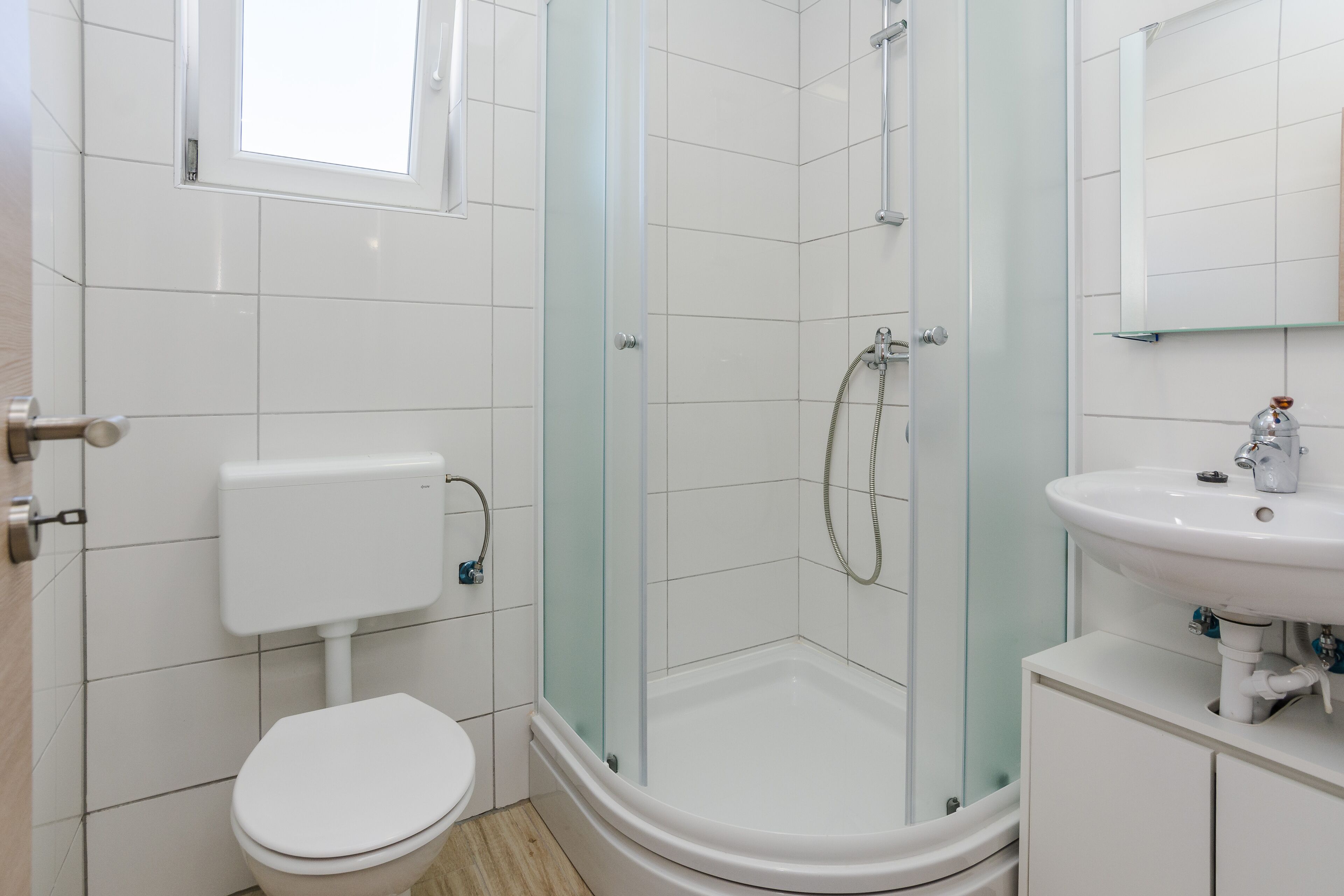 A modern bathroom with a glass-enclosed shower, a white toilet, and a sink with a mirror above it.