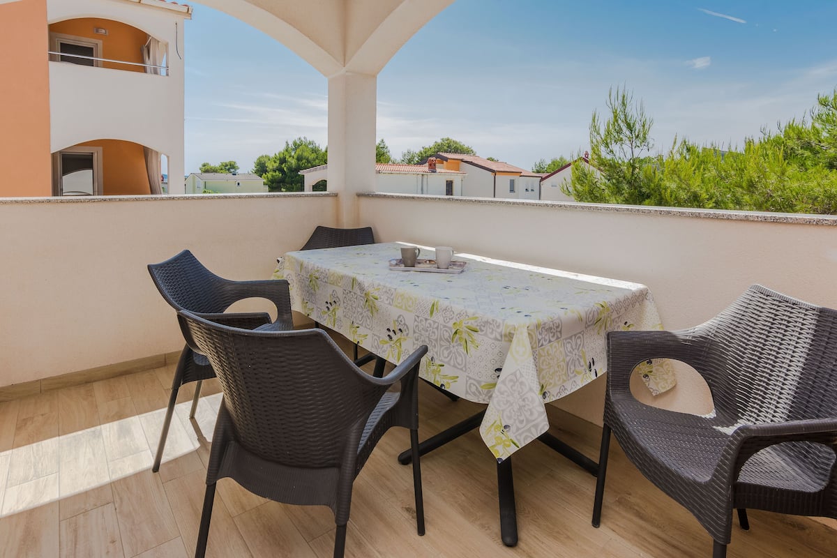 Un balcon avec une table et des chaises, donnant sur un quartier résidentiel avec des maisons et des arbres.