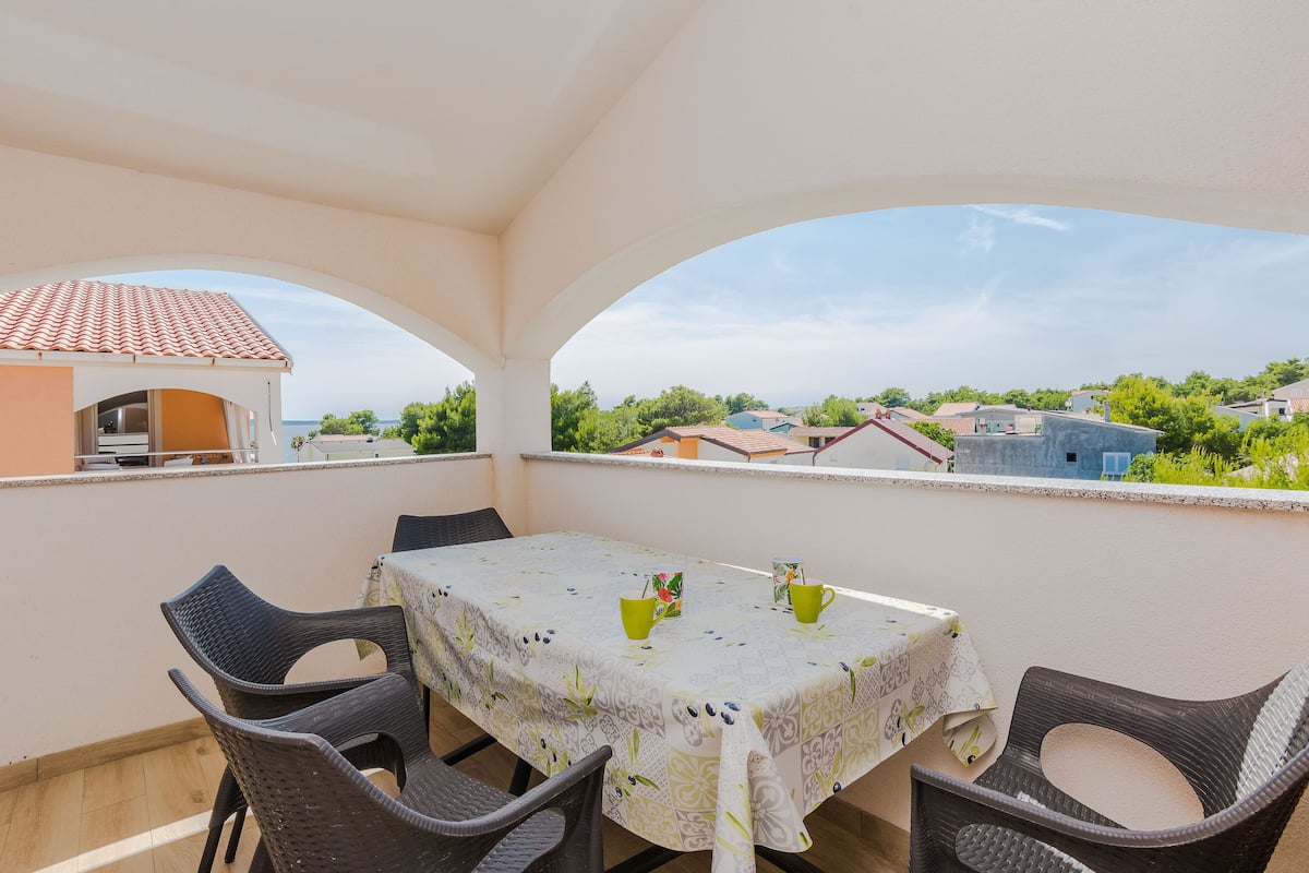 Un balcon avec une table et des chaises, une vue sur les maisons et un ciel dégagé.