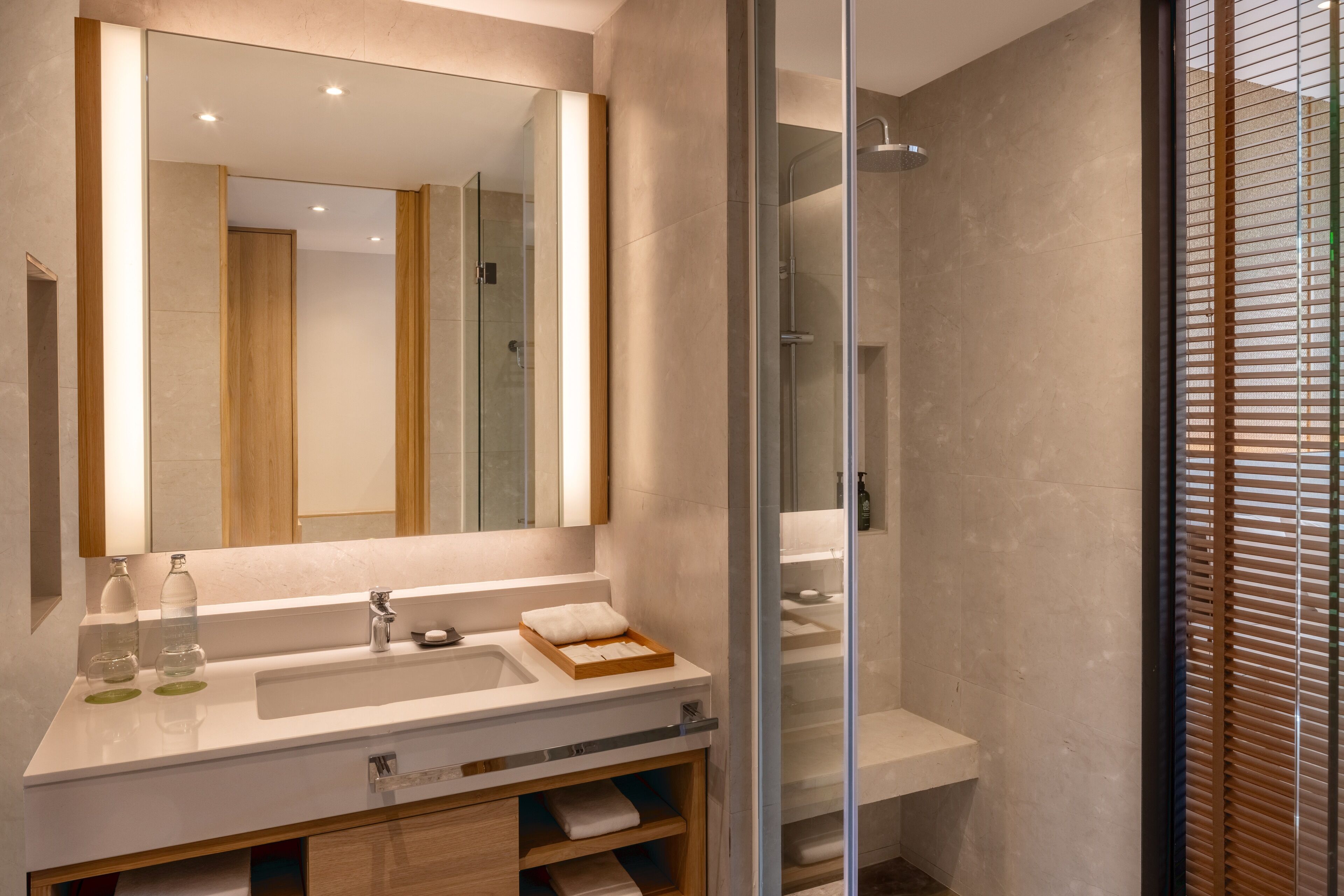 A modern bathroom with a large mirror, a white sink, and a glass-enclosed shower.