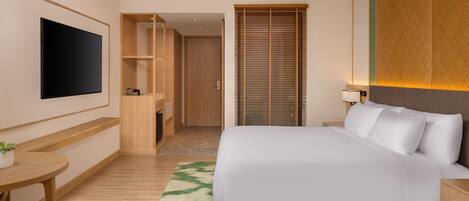 A modern hotel room with a large bed, a flat-screen TV mounted on the wall, a wooden desk, and a small table with a plant.
