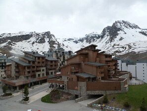 Uma pousada de montanha com vários edifícios de madeira, um pátio central e montanhas cobertas de neve ao fundo.