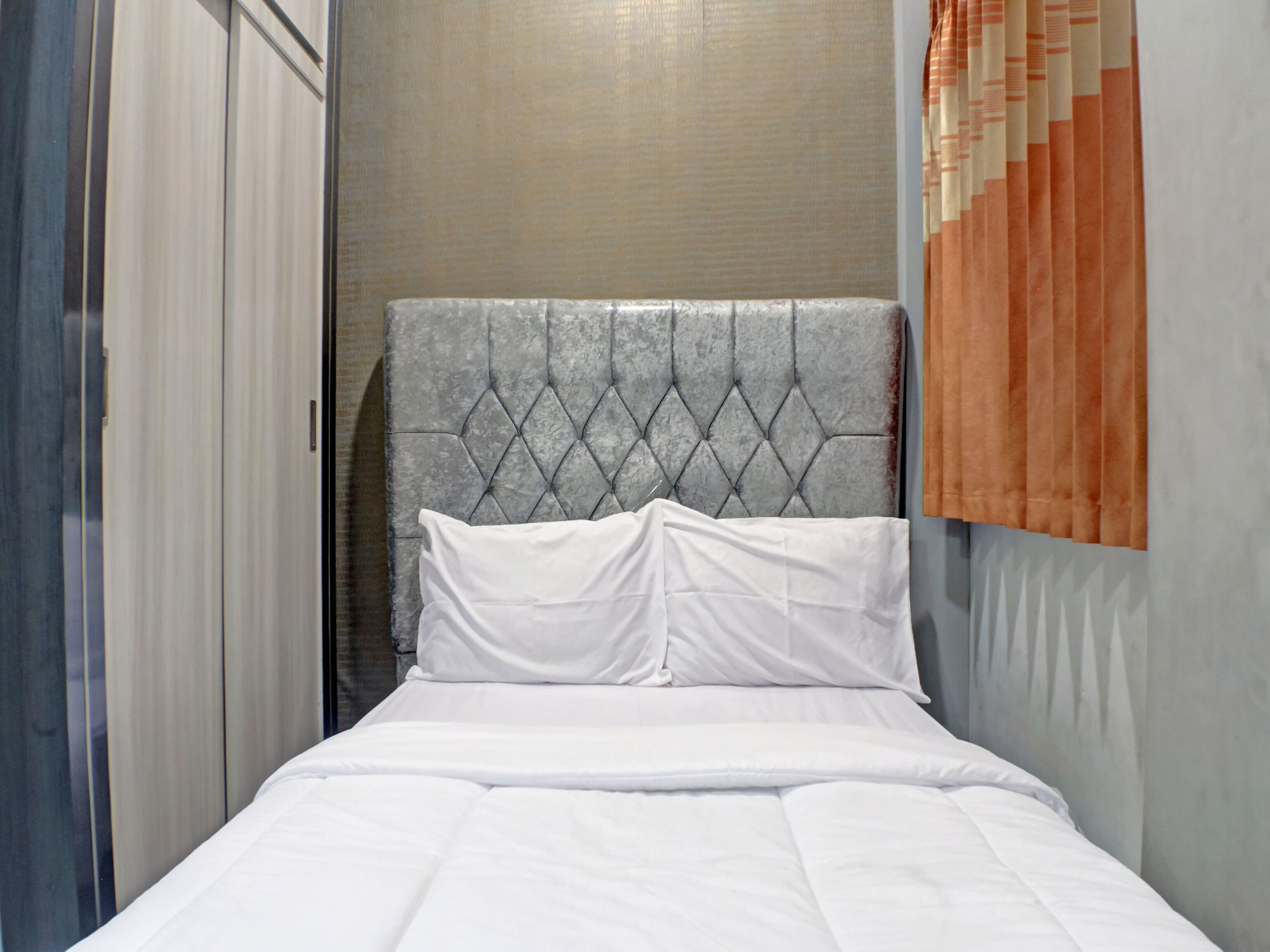 A neatly made bed with a tufted headboard, a white pillow, and a white duvet.
