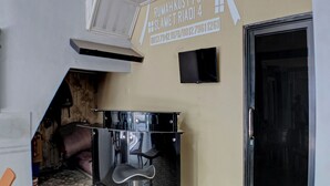 A corner of a room with a black bar stool, a television mounted on the wall, and a door to the right. - OYO Life 92830 Homestay Slamet Riadi Iv (Bandar Lampung)