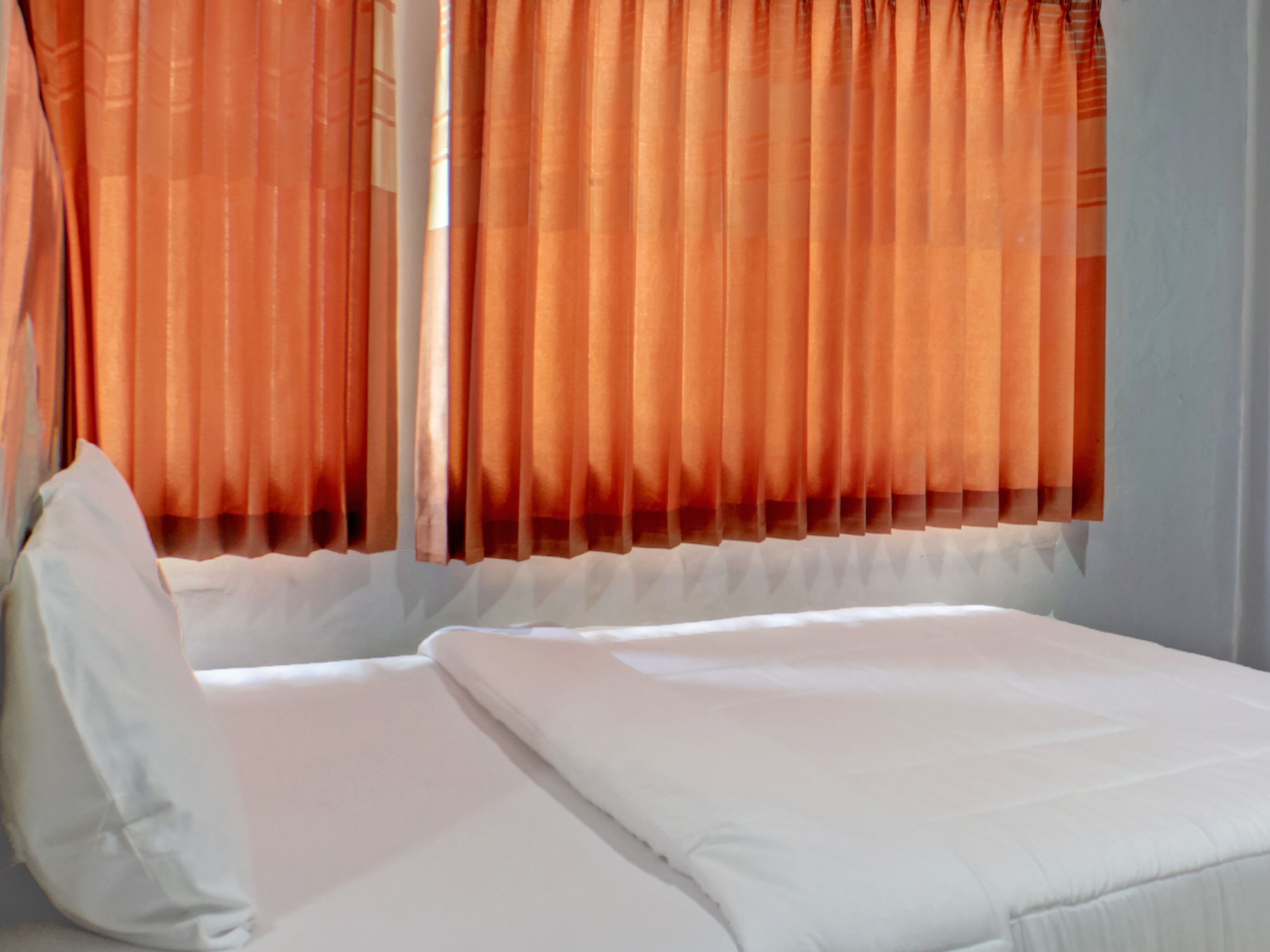 A bed with white bedding in a room with orange curtains.