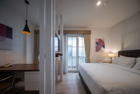 Una habitación de hotel con cama, mesita de noche, lámpara y vistas al balcón exterior.