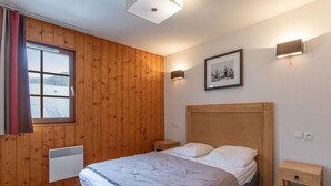 A bedroom with a wooden paneled wall, a bed with a headboard, bedside tables, a wall-mounted light, and a window with curtains.