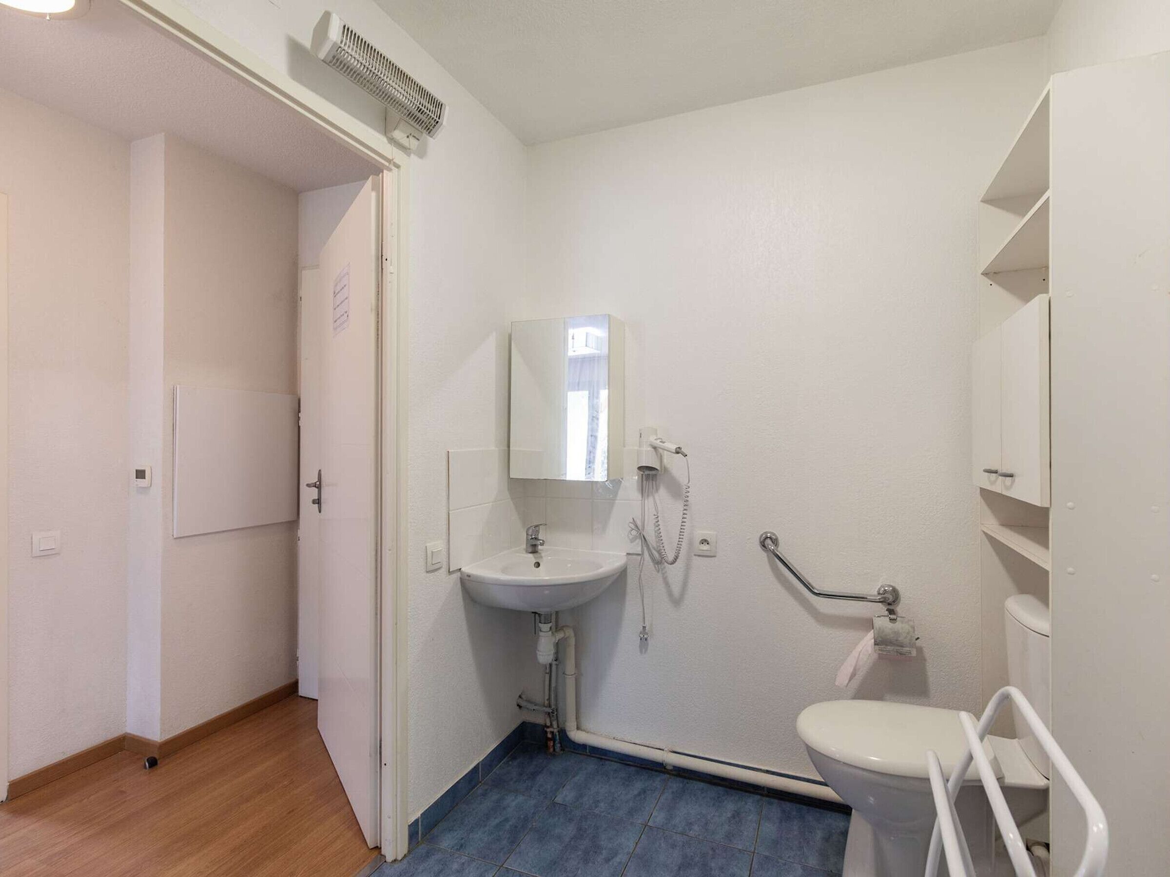 A small, clean bathroom with a sink, mirror, toilet, and a shower area.