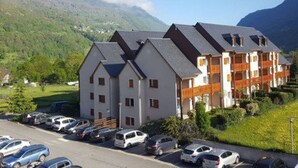 A multi-story hotel with a parking lot in front, surrounded by greenery and mountains.