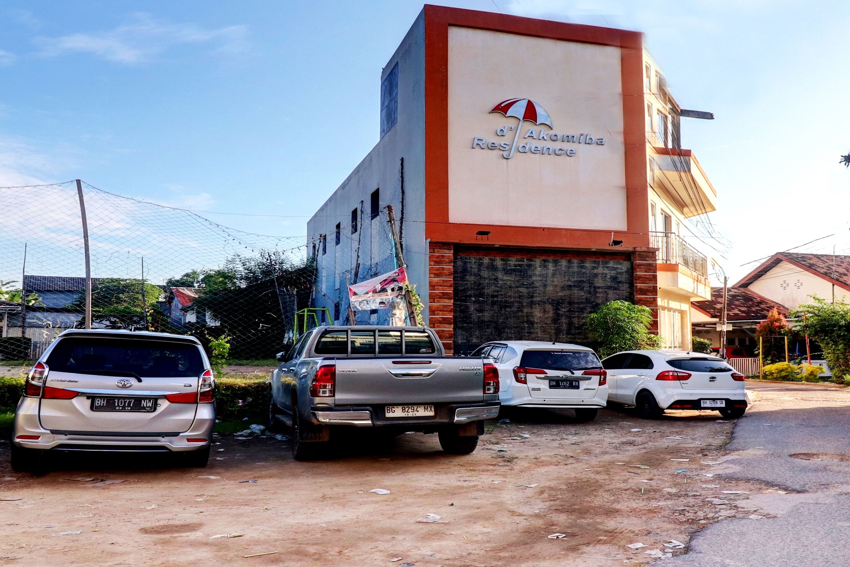 A building with a sign reading "d'Akouloua Residence" and several parked vehicles in front.